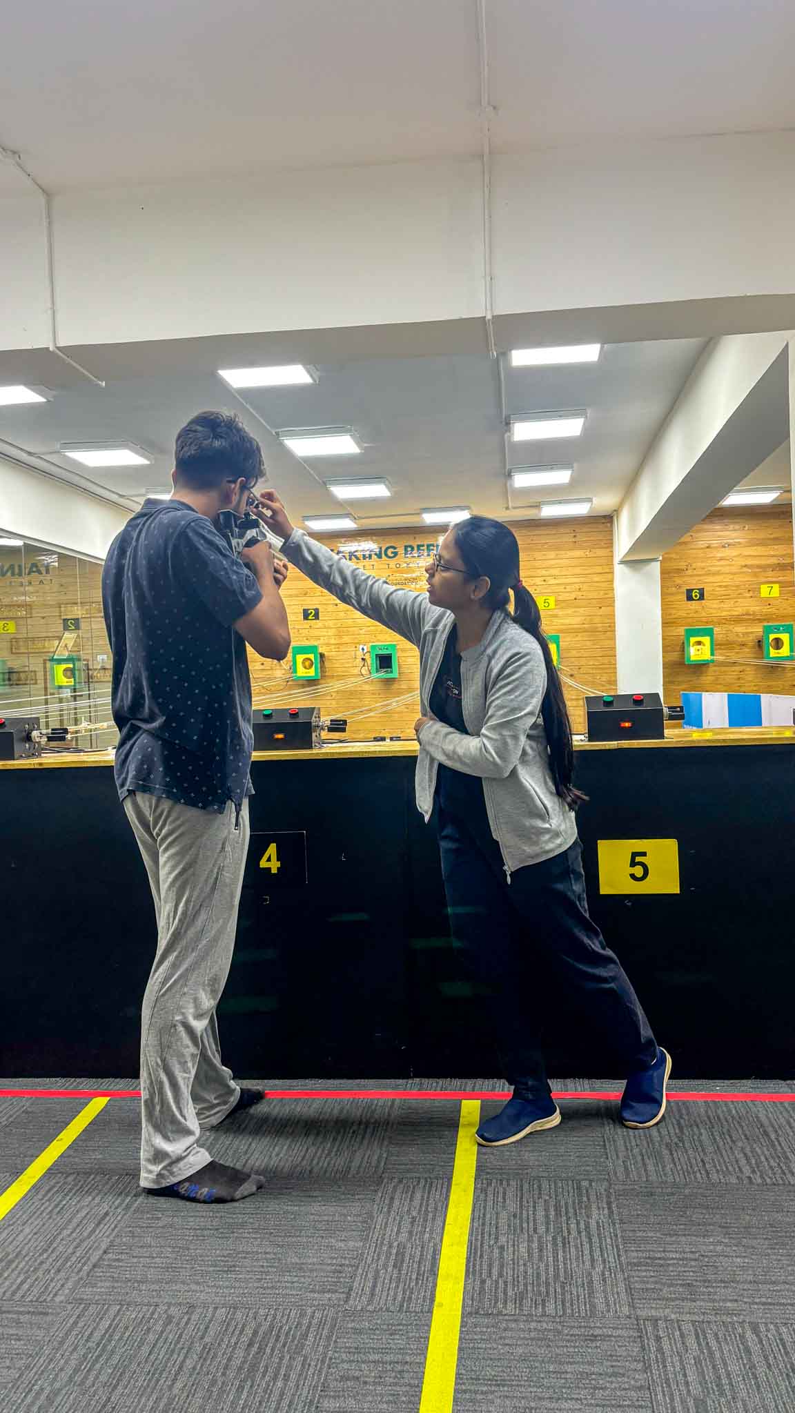 A male shooter concentrates on aiming a rifle while receiving instructions at Bengaluru's best shooting range.